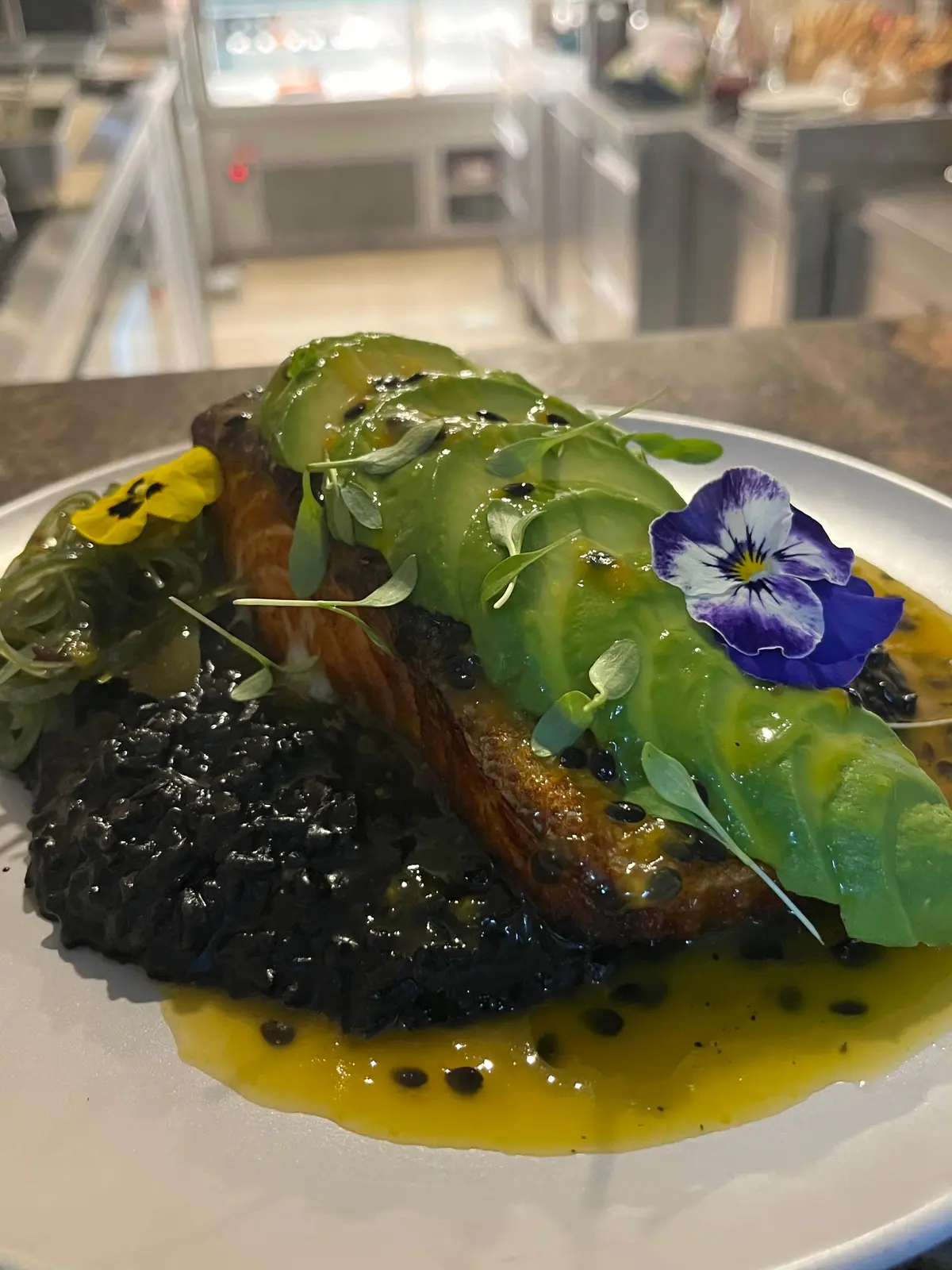 Salmão com abacate, arroz negro e flores comestíveis.