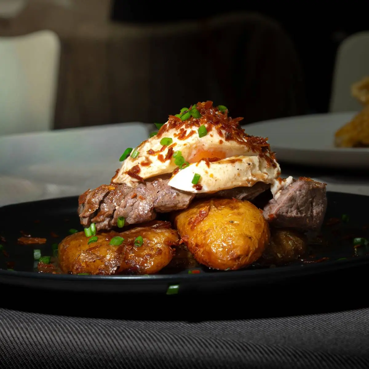 Bife com ovo escalfado, batatas assadas e cebolinho.